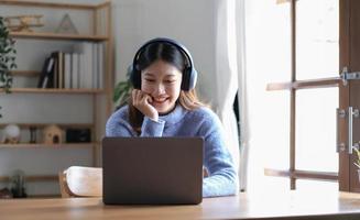 glad skön asiatisk kvinna bär hörlurar och se till digital läsplatta på video kallelse möte och studie uppkopplad på de internet. foto