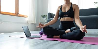stänga upp av hand kvinna håller på med lotus yoga övningar på yoga matta med Träning uppkopplad på de läsplatta på Hem morgon, begrepp av avslappning och meditation foto