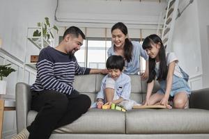 lycklig asiatisk härlig thailändsk familjeomsorg, pappa, mamma och små barn har roligt när de leker med färgglada leksaksblock tillsammans på soffan i det vita vardagsrummet, fritidshelgen och livsstilen för välbefinnande i hemmet. foto