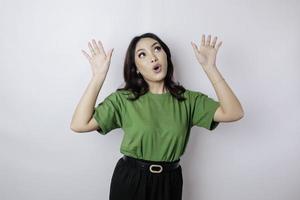 chockade asiatisk kvinna bär grön t-shirt pekande på de kopia Plats upside henne, isolerat förbi vit bakgrund foto