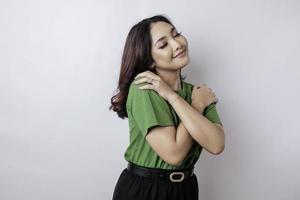 ung skön asiatisk kvinna bär tillfällig grön t-shirt över vit bakgrund kramas själv Lycklig och positiv, leende självsäker. själv kärlek och själv vård foto