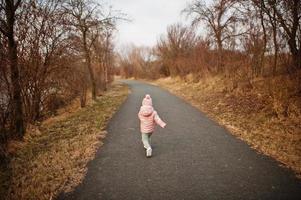 baksidan av rinnande flicka i rosa jacka på vägen. foto