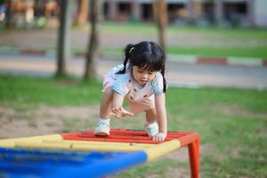 söt asiatisk flicka leende spela på skola eller dagis gård eller lekplats. friska sommar aktivitet för barn. liten asiatisk flicka klättrande utomhus på lekplats. barn spelar på utomhus- lekplats. foto