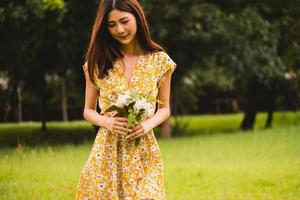 skön kvinna i gul klänning innehav blommor stående på gräs i de parkera foto