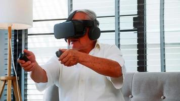 asiatisk senior man har roligt spelar video spel med virtuell verklighet glasögon på Hem. foto
