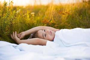 flicka sover på säng i gräs, ljuv sträckor och gäspar sömnig, Bra morgon- i färsk luft. miljövänlig, friska sova, skydd från myggor, rena natur, ekologi, barns hälsa foto