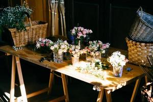 långt träbord med olika buketter av vackra blommor. behagligt doftande rosor som står i glas. tomma träryggar. skapandet av ett knippe blommor. rosor arrangerade för dekoration foto