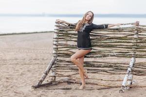 förtjusande smal ung kvinna modell står på strand nära trä- därmed, demonstrerar smal ben, återskapar ensam på havet, känner avslappning och frihet. sommar högtider och avslappning begrepp foto