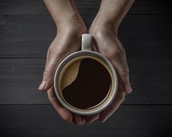 varm kaffe kopp i händer med kaffe bönor på de trä- tabell foto