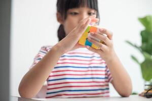 asiatisk liten söt flicka innehav rubiks kub i henne händer. rubiks kub är en spel den där ökar de intelligens av barn. foto