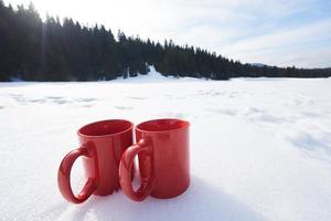 två röd kupper av varm te dryck i snö på vinter- foto