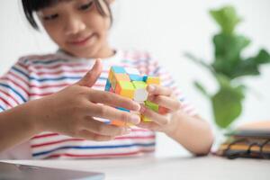 asiatisk liten söt flicka innehav rubiks kub i henne händer. rubiks kub är en spel den där ökar de intelligens av barn. foto