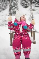 liten flicka på snöig vinter- dag gunga i parkera foto