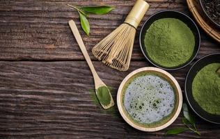 japansk organisk matcha grön te pulver i skål med tråd vispa och grön te blad på trä- bakgrund, organisk produkt från de natur för friska med traditionell stil foto