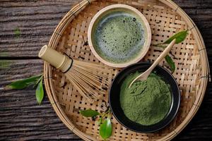 japansk organisk matcha grön te pulver i skål med tråd vispa och grön te blad på trä- bakgrund, organisk produkt från de natur för friska med traditionell stil foto