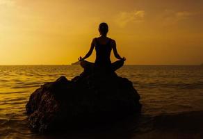 silhuett ung kvinna utövar yoga på stranden vid solnedgången. foto