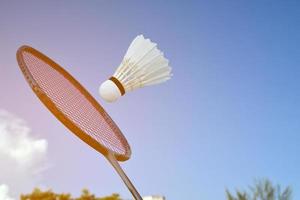 badminton racket och badminton fjäderboll mot molnig och blå himmel bakgrund, utomhus- badminton spelar begrepp. selektiv fokus på racket. foto