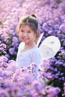 söt liten leende flicka ha på sig en magi balett fe- kostym i skön lila av margaret blommor fält. foto