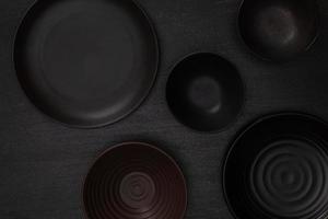 grupp av tömma tom svart keramisk runda skålar och plattor på svart sten blackground, topp se av traditionell handgjord köksutrustning begrepp foto