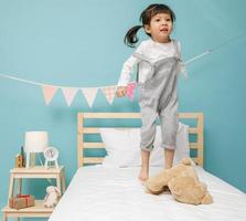 barn flicka spelar på de trä- säng i henne sovrum, Lycklig asiatisk barn liten flicka Hoppar på de säng, Lycklig familj begrepp foto