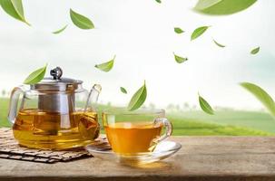 kanna och varm te glas kopp med flygande virvla grön te löv i de luft i te plantager, friska Produkter förbi organisk naturlig Ingredienser begrepp, foto