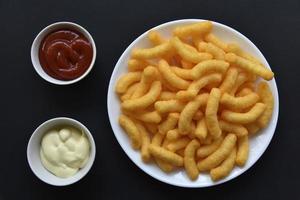 paprika majs pommes frites med sås på en svart bakgrund. salt mellanmål av majs snacks närbild. foto