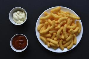 paprika majs pommes frites med sås på en svart bakgrund. salt mellanmål av majs snacks närbild. foto