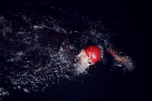 triathlon idrottare simmar i mörk natt iklädd våtdräkt foto