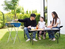 familj förälder far mor son flicka bar-bq utegrill biff grill mat äter lunch middag Lycklig leende livsstil Semester semester roligt njut av utomhus- trädgård naturlig fest sommar foto