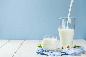 häller en glas av mjölk på en vit trä- tabell på en blå bakgrund, gott, näringsrik och friska mejeri Produkter foto