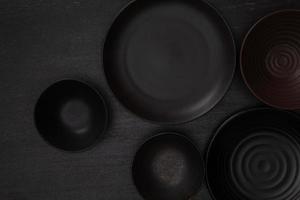 grupp av tömma tom svart keramisk runda skålar och plattor på svart sten blackground, topp se av traditionell handgjord köksutrustning begrepp foto