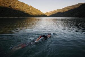 triathlon idrottare simmar på sjön i soluppgången bär våtdräkt foto