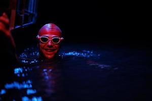 äkta triathlete simmare har en ha sönder under hård Träning på natt neon gel ljus foto