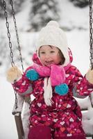 liten flicka på snöig vinter- dag gunga i parkera foto
