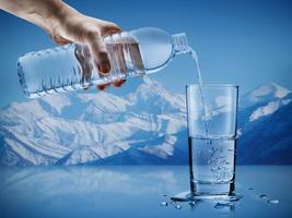 hand häller mineral vatten från flaska in i en glas med vatten droppar i de isberg bakgrund, sjukvård och skönhet hydratisering begrepp foto