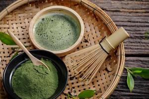 japansk organisk matcha grön te pulver i skål med tråd vispa och grön te blad på trä- bakgrund, organisk produkt från de natur för friska med traditionell stil foto