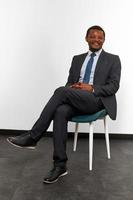 leende afrikansk amerikan svart man i företag kostym Sammanträde på stol med korsade fingrar foto