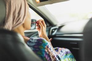 kvinna ser i bak- se spegel målning henne mun håller på med applicering göra upp i bil. foto