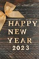 Lycklig ny år 2023 text på trä- bakgrund med gyllene rosett. festlig hälsning kort för vinter- högtider foto