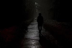 silhuett av man på natt i parkera. man promenader ensam på väg i kväll. foto