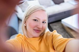 Häftigt ung kvinna med blond hår tar selfie. stänga upp Foto av skön flicka tar selfies hand ärm innehav kamera sändningar blog ha på sig tillfällig Tröja pullover