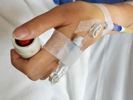 makro bild av patient hand med infusion nål och intravenöst rör för intravenös infusion uppsättning på hand tryckande nödsituation knapp på säng. foto