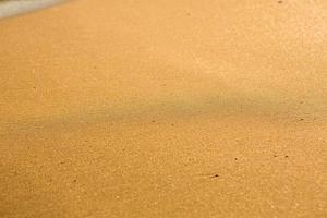 bakgrund med gyllene sand på de kust av de ö av Kreta. abstrakt yta med sand och klar hav vatten för text. foto