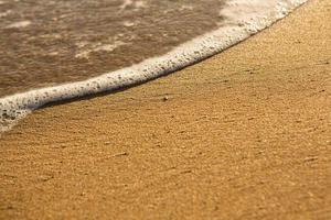 bakgrund med gyllene sand på de kust av de ö av Kreta. abstrakt yta med sand och klar hav vatten för text. foto