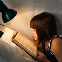 flicka läsning bok på säng på natt foto