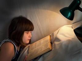 tonåring flicka läsning bok på säng på natt foto