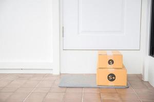 kartong paket låda nära dörr på golv. uppkopplad handla, lådor levereras till din främre dörr. lätt till stjäla när ingen är Hem. paket i kartong låda på tröskel. leverans service foto
