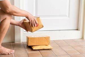 kvinna samlar paket på dörr. låda nära dörr på golv. uppkopplad handla, lådor levereras till din främre dörr. lätt till stjäla när ingen är Hem. paket i kartong låda på tröskel. leverans service foto