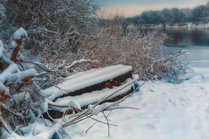 de båt lögner på de Bank av de flod i vinter- foto