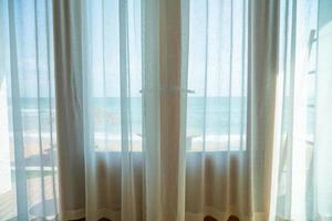 ridå och glas fönster med hav strand se utanför foto